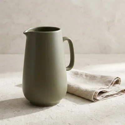 Concept ceramic table jug on a pale surface beside folded linen.
