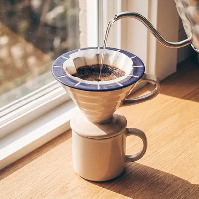 Concept dripper on a mug by a sunny window, with water pouring from a kettle.